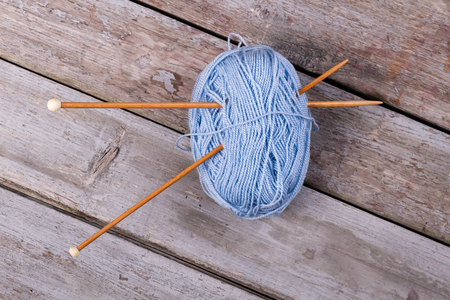 Blue yarn with wooden knitting needles. Skein of blue thread on gray wooden background.