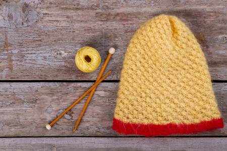 Yellow knitted woolen hat with red trim. Fluffy hat with thread and wooden spokes.の写真素材