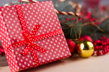 Present for Christmas celebration. Close up on red gift box with white stars pattern in front of glass balls and fir branch.の写真素材