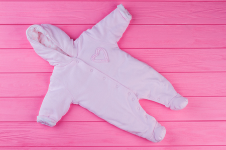 Baby girl fleece coverall, top view. Layette hooded pink baby cloth in pink wood background.の写真素材