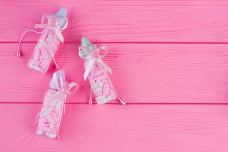 Three baby bottles full of pills. Top view, flat lay. Pink wooden desk background.の写真素材