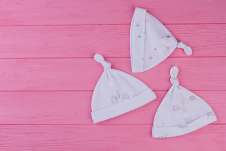 Set of hats for newborn, top view. Three cotton knot hats for newborn girl on pink wooden...