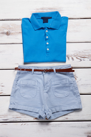 Blue polo shirt and light jeans shorts on a white wooden background.の写真素材