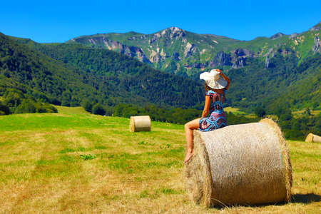 woman with dress and hat sitting on bale of hayの写真素材