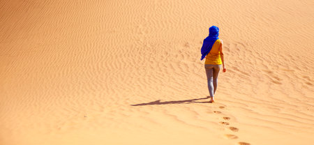 Woman tourist walking in the sahara desert with blue turbanの写真素材