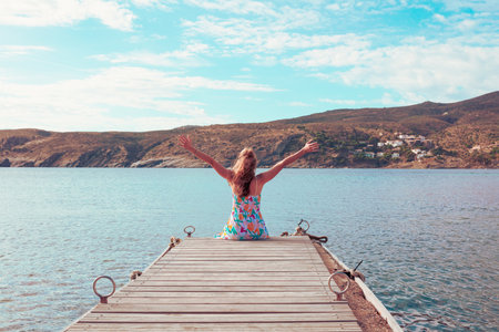 Woman arms raised sitting on wooden pierの写真素材