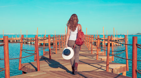 Woman walking on wooden pier looking at the seaの写真素材
