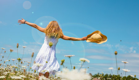 Woman wearing white dress dancing in a field with flowers and blue sky- freedom, active, healthy conceptの写真素材
