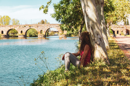 Woman tourist sitting and looking at ancient roman bridge in Merida city landscape- Estramaduraの写真素材