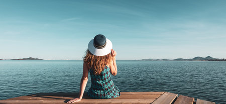 Woman sitting on wooden pier looking at the seaの写真素材