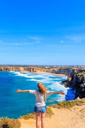 Woman with outstretched arms enjoying the wind and fresh air in front of atlantic ocean- Portugalの写真素材