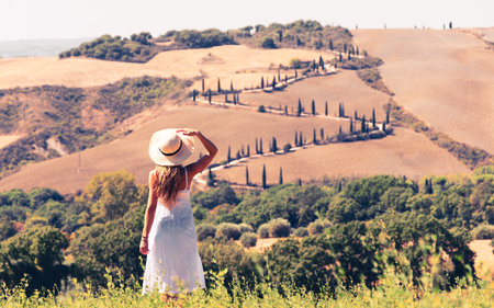Attractive young female with hat and white dress traveling in Tuscan landscape- Italyの写真素材