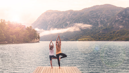 Mother and child doing yoga on pier in front of beautiful lake- Bohinj lake in Sloveniaの写真素材