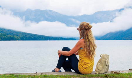 Thoughtful Woman sitting and looking at lake with alps mountain with mistの写真素材