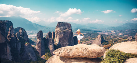 Meteora, Greece-Woman in white dress enjoying panorama of mountain scenery of rocks and monasteries.の写真素材
