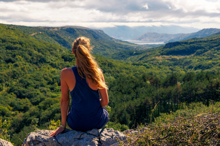 Woman sitting on rock enjoying mountains and forest viewの写真素材