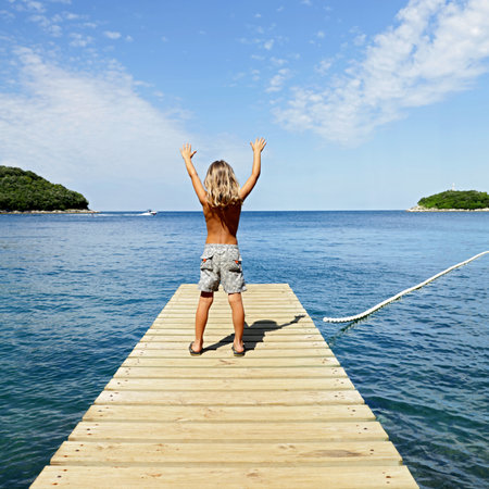 Happy little boy with arms up, standing on wooden pier enjoying the sea- Travel, vacation, summer, freedom conceptの写真素材