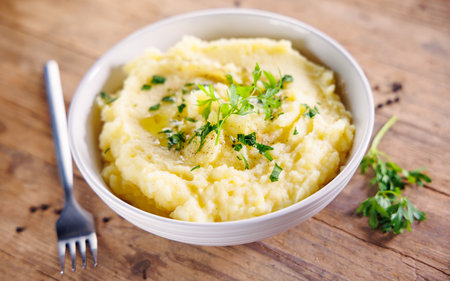Bowl of mashed potatoes with butter and parsley on wooden background. Perfect for comfort food and...