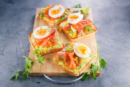 Avocado, smoked salmon, and egg on toast served on a wooden board. Perfect for healthy breakfasts...