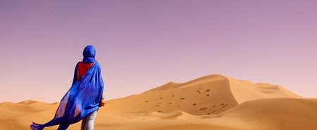 Rear view of young woman with blue waving textile in the sahara desert at sunsetの写真素材