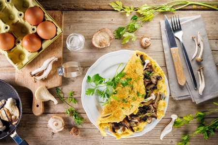 fluffy omelet with mushrooms on plate with ingredients on wooden backgroundの写真素材