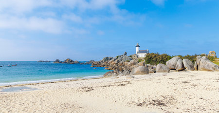 A scenic view of a white lighthouse on a rocky coastline overlooking a sandy beach with turquoise waters under a blue sky, capturing the beauty of the French coast. brittanyの写真素材