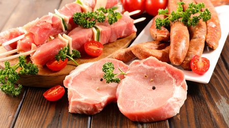 raw pork chop, sausage and skewer with cherry tomato and parsley on wooden table, ready for grilling, barbecue preparation scene with fresh meatの写真素材