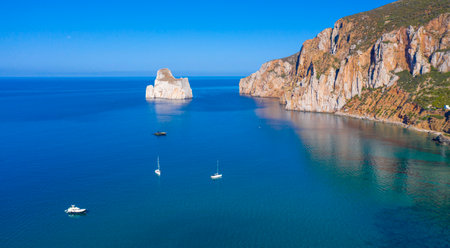Panoramic view of Masua beach in Sardinia, Italy, with crystal-clear turquoise water, boats anchored near the coast, and the iconic Pan di Zucchero rockの写真素材