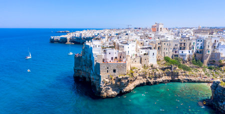 white cliffside village of Polignano a Mare in Puglia, Italy, historic stone house above turquoise water, swimmers and sailboats in summerの写真素材