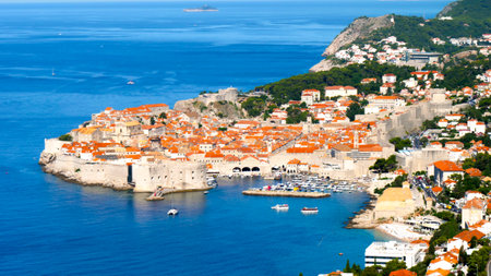 aerial view of a fortified coastal town with orange roofs, stone wall and marina, surrounded by clear blue sea and green hills, summer atmosphere in dubrovnikの写真素材