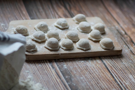 Cooking dumplings. On the table are dumplings on a wooden board, next to a rolling pin of dough.