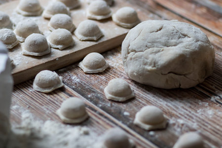 Cooking dumplings. On the table are dumplings on a wooden board, next to a rolling pin of dough.の写真素材