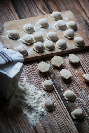 Cooking dumplings. On the table are dumplings on a wooden board, next to a rolling pin of dough.の写真素材