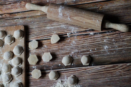 Cooking dumplings. On the table are dumplings on a wooden board, next to a rolling pin of dough.の写真素材