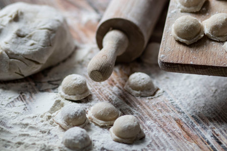 Cooking dumplings. On the table are dumplings on a wooden board, next to a rolling pin of dough.の写真素材