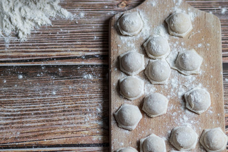 Cooking dumplings. On the table are dumplings on a wooden board, next to a rolling pin of dough.の写真素材