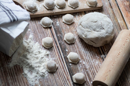 Cooking dumplings. On the table are dumplings on a wooden board, next to a rolling pin of dough.の写真素材