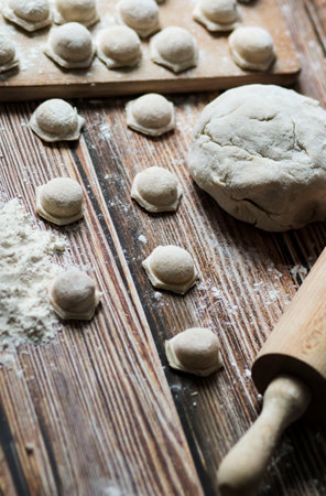 Cooking dumplings. On the table are dumplings on a wooden board, next to a rolling pin of dough.の写真素材