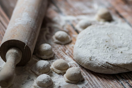 Cooking dumplings. On the table are dumplings on a wooden board, next to a rolling pin of dough.の写真素材