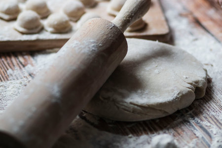 Cooking dumplings. On the table are dumplings on a wooden board, next to a rolling pin of dough.の写真素材