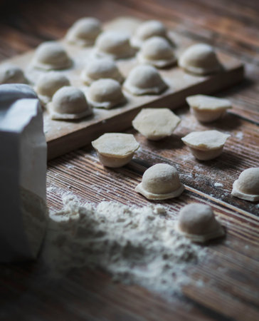 Cooking dumplings. On the table are dumplings on a wooden board, next to a rolling pin of dough.の写真素材