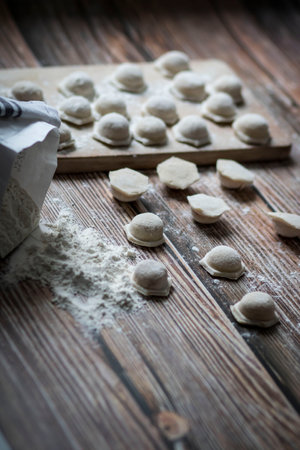 Cooking dumplings. On the table are dumplings on a wooden board, next to a rolling pin of dough.の写真素材