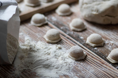Cooking dumplings. On the table are dumplings on a wooden board, next to a rolling pin of dough.の写真素材