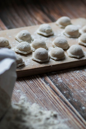 Cooking dumplings. On the table are dumplings on a wooden board, next to a rolling pin of dough.の写真素材