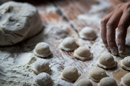 Cooking dumplings. On the table are dumplings on a wooden board, next to a rolling pin of dough.の写真素材