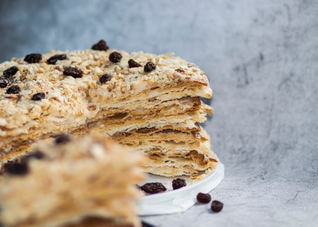 Napolion cake. A piece of cake on a black plate, decorated with raisins. Stands on a table with a gray backgroundの写真素材