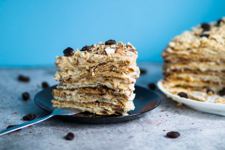 Napolion cake. A piece of cake on a black plate, decorated with raisins. Stands on a table with a gray backgroundの写真素材