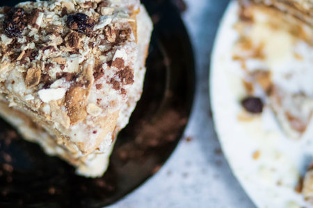 Napolion cake. A piece of cake on a black plate, decorated with raisins. Stands on a table with a gray backgroundの写真素材