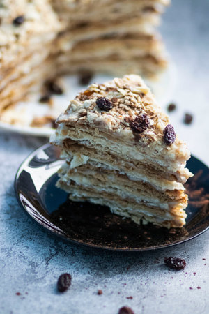 Napolion cake. A piece of cake on a black plate, decorated with raisins. Stands on a table with a gray backgroundの写真素材
