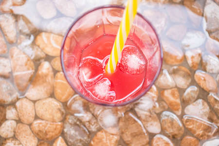Fruit cold juice in summer. Cold juice with ice stands on wet pebbles